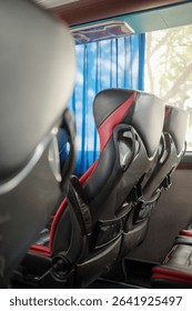 View inside a modern bus or coach, showing rows of black and red passenger seats. Blue curtains and a window with natural light are visible.
