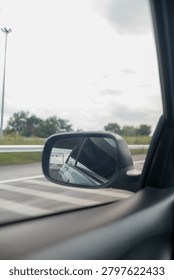 View from inside a moving car, capturing the highway, road lines, and another vehicle reflected in the side mirror.