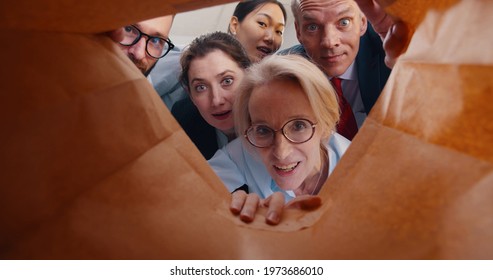 View From Inside Paper Bag Of Business People Looking Inside. Hungry Business Team Opening Delivery Bag With Takeaway Food For Lunch Working In Modern Office