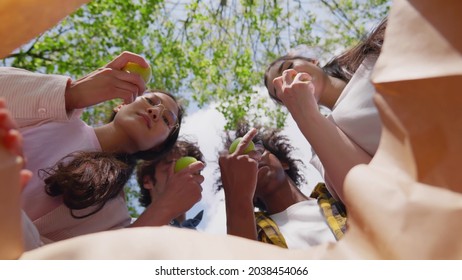 View From Inside Paper Bag Of Multiethnic Friends Take Green Apple And Bite Outdoors. Diverse Students Eat Healthy Snack For Lunch In Park