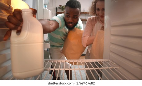 View From Inside Of Refrigerator Of Multiracial Couple Unpack Online Home Food Delivery. Happy diverse man and woman putting groceries in refrigerator - Powered by Shutterstock