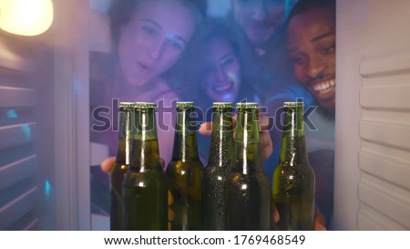 View from inside steamy fridge of young happy diverse people opening refrigerator taking bottles with cool beer celebrating event at house party together