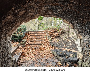 View from inside a stone archway looking out onto park steps covered in fallen autumn leaves in London