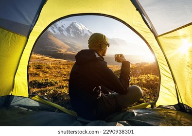 View from inside a tent of hiker drink hot tea and looking to the mountains valley with ice glacier landscape at sunset during trekking in Central Asia Kazakhstan, Almaty