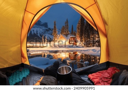 View from inside a tent of tourist relaxing and looking to the wooden lodge glowing on Emerald Lake in winter at Yoho national park, BC, Canada