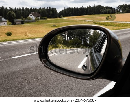 View into the car side mirror on the left side. The street in the rural area is empty. The blind spot is not visible in the rearview mirror.
