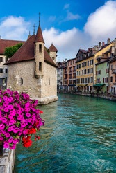 View Of The Island's Medieval Palace In The Middle Of The River That Runs Through The Center Of Annecy In France With Flowers In The Foreground - Selective Focus
