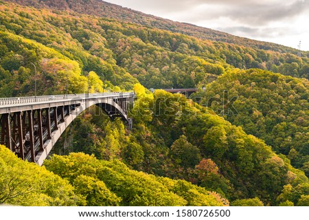View of Jogakura Bridge with the beautiful mountain forest of autumn colors in Towada Hachimantai National Park, Akita Prefecture, Japan.