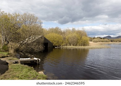 View from just off the West Highland Way walking trail of a boathouse on the shore of Craigallian Loch with Dumgoyne hill in the background. North of Milngavie, East Dunbartonshire, Central Scotland. - Powered by Shutterstock