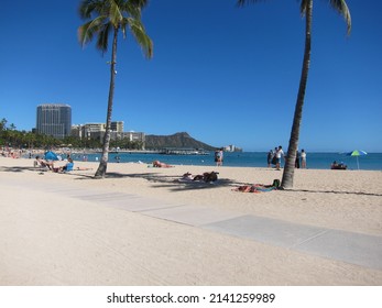 View of Kahanamoku Beach, Waikiki. View of the horizon with palm trees, Diamond Head mountain summit, clear blue sky, the skyline, and a walkaway across the beige sand. Oahu, Hawaii. - Shutterstock ID 2141259989