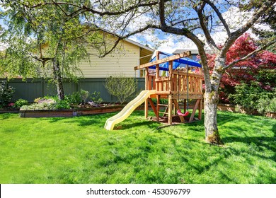 View Of Kids Playground In Green Backyard Garden With Birch Trees And Flower Bed.