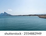 View of La Linea de la Concepcion coastline with Gibraltar Rock in the background. Calm sea water in the foreground, city with houses and beaches, clear sky.