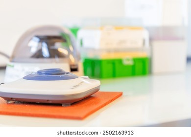 View of a laboratory vortex mixer. A small mini centrifuge in the background and plastic boxes with pipet tips. Copy space available. Background for science, science education poster, publicity. - Powered by Shutterstock