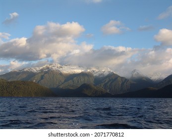 A view of a lake with a mountain range in the background and cloudy sky above