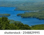 View of Lake Sunapee from the top of Mt. Sunapee in Newbury, New Hampshire in summertime, with blue waters of the lake below.