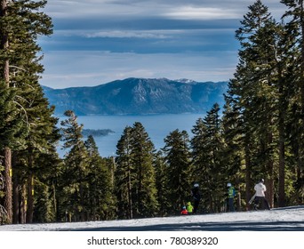 A View Of Lake Tahoe From The Top Of Northstar Ski Resort, In The Sierra Nevada Mountain Range In Truckee, California, With Pine Trees Framing The Lake, As Skiers Ski Down The Ski Slopes. 