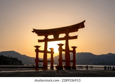 View of landmark Shinto Shrine or Torii Gate of Miyajima (Itsukushima) Island, Japan, during low tide sunset and sun shining through gate (translation text on shrine: Itsukushima Shrine)