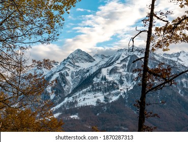 View Of Landscape Through Autumn Forest To The High Mountains In The Snow. Transition From Autumn To Winter.