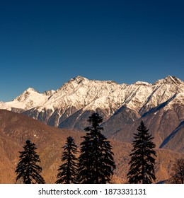 View Of Landscape Through Autumn Forest To The High Mountains In The Snow. Transition From Autumn To Winter.