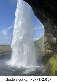View of a large waterfall cascading down with a clear blue sky and rocky cliffside visible.