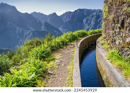 View from Levada do Norte on the portuguese island of Madeira. Spring in Madeira. Levada irrigation canal. Hiking in Madeira. Narrow path next to the levada. Green mountains in background. 