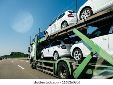 View of lgeneric white long truck trailer transporting new cars and riding on highway in sunlight under blue sky