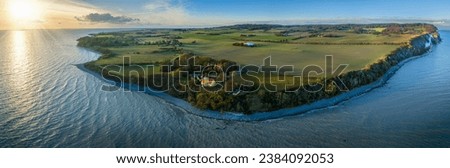 View of Møn lighthouse, distinguished by its striking yellow tower, white gallery, and vibrant red-roofed lantern and pebble beach at Møn’s south-eastern point where the majestic Møns Klint rises.