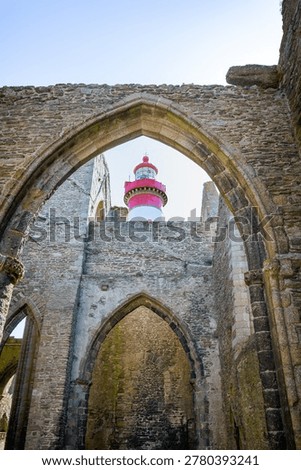 View of Saint‑Mathieu lighthouse framed by Gothic stone arches of medieval abbey ruins Plougonvelin Finistere Brittany France showing contrast between ancient architecture and modern maritime structure