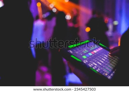 View of lighting technician with tablet, operator controlling sound and light during live event concert on stage show broadcast, technician with professional equipment, working on mixing console