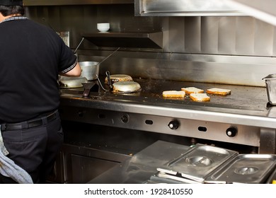 A View Of A Line Cook Attending A Stove And Griddle Area. Slices Of Bread Are Toasting On The Griddle, In A Restaurant Kitchen Setting. 