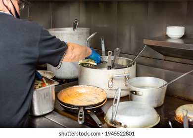 A View Of A Line Cook Managing Food Prep In A Busy Restaurant Kitchen Cooking Area, Featuring Stockpots, Grilled Food And Clutter.