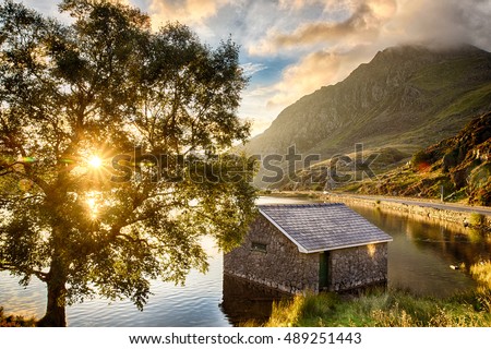 View of Llyn Ogwen Lake at sunrise with blue sky. House in the lake and tree.