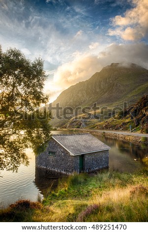 View of Llyn Ogwen Lake at sunrise with blue sky. House in the lake and tree.
