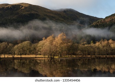 View Of The Loch Lomond Under A Blue Sky In A Misty Morning Where Trees On The Lakeside And Low Clouds Are Reflected On The Lake's Calm Water A In Trossachs National Park, Scotland, UK