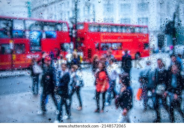 view of \
London street with red double decker bus through the glass of a car\
covered with raindrops. Focus on\
drops