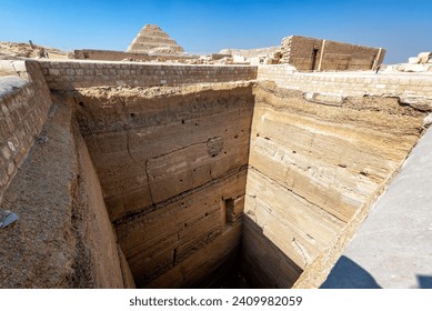 View of a long vertical shaft at Saqqara, Egypt with the Pyramid of Djoser in the background