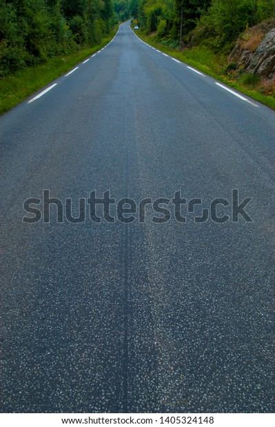 View\
of a long, wet road with white stripes on the\
sides.