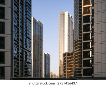View looking up between dense high-rise residential and commercial buildings toward a brightly illuminated skyscraper. The scene represents rapid urban development, modern architecture, economic growth, and metropolitan living.