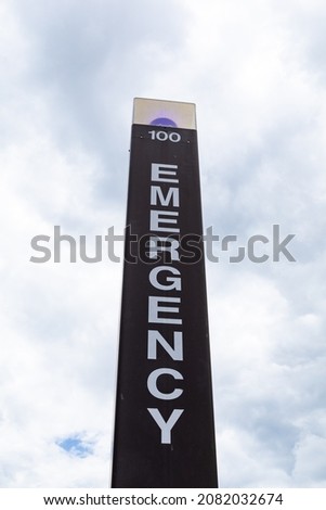 View looking up at a blue light emergency call box against a cloudy sky, vertical aspect