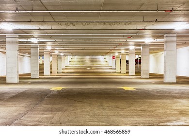 View Looking Down The Length Of An Empty Undercover Parking Garage Illuminated By Overhead Strip Lights With Forward Pointing Arrows On The Concrete Floor