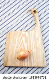 A view looking down on a large knife and onion on a worn butcher block cutting board.