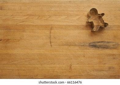 A view looking down on a single metal gingerbread man cookie cutter on a worn butcher block cutting board