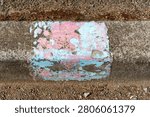 View looking down onto a small section of worn and eroded paint in colours of pink and pale blue painted on to the gutter in a suburban street in Sandy Bay, Tasmania, indicating an access point nearby.