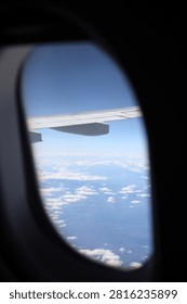 View looking through an airplane window showing the wing and fluffy white clouds
