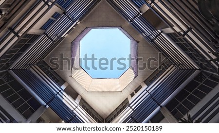 A view looking up through an octagonal open space in the center of a building, with the blue sky visible above. The building's structure features metal bars and glass windows.