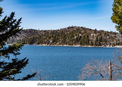 View Looking Towards The Lake Arrowhead North Shore With A Boat, Blue Sky, Green Trees, Hills And Blue Rippling Water