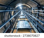 View looking upward from inside a circular elevator shaft, revealing repeating floors with elevator doors on each level. The perspective emphasizes geometric symmetry, vertical depth, and the architectural structure of the building.