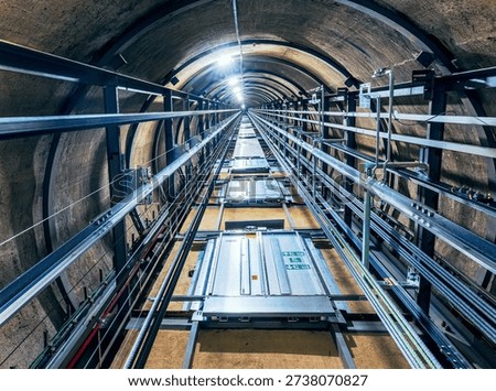 View looking upward from inside a circular elevator shaft, revealing repeating floors with elevator doors on each level. The perspective emphasizes geometric symmetry, vertical depth, and the architectural structure of the building.
