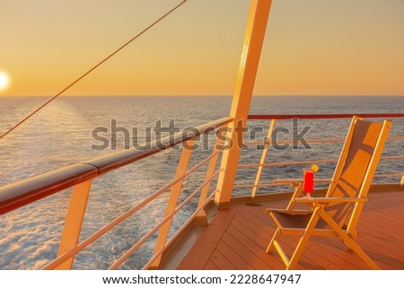View from a lounge chair with a cocktail on the deck of a cruise ship at sunset in the wake of the cruise ship. View from the stern of the ship.	