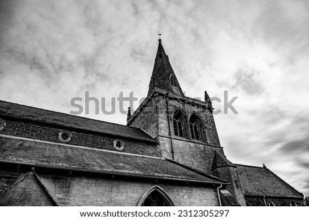 View from a low angle of a Victorian English church looking upwards towards the steeple with a textural cloudy sky behind